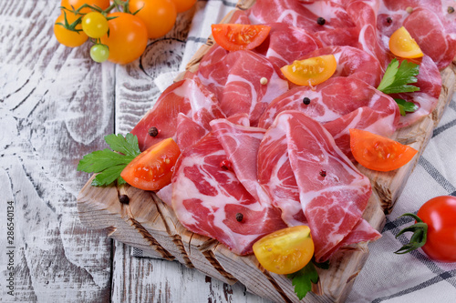 Thin slices of Italian cold cut pork Coppa and cut cherry tomatoes on wooden board