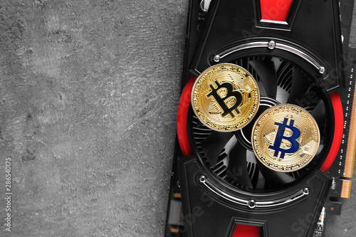 Bitcoins and video card on grey background, space for text
