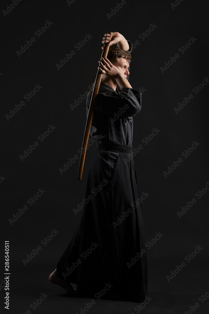 Kendo guru wearing in a traditional japanese kimono is practicing martial art with the shinai bamboo sword against a black studio background. Kendo guru wearing in a traditional japanese kimono is practicing martial art with the shinai bamboo sword against a black studio background.