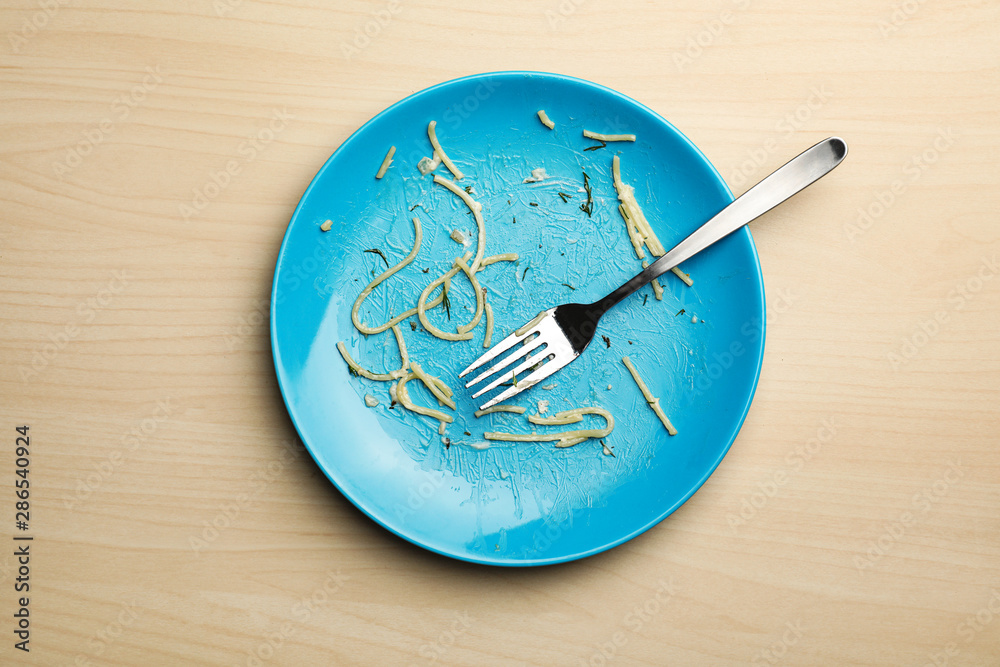Dirty plate with food leftovers and fork on wooden background, top view Dirty plate with food leftovers and fork on wooden background, top view