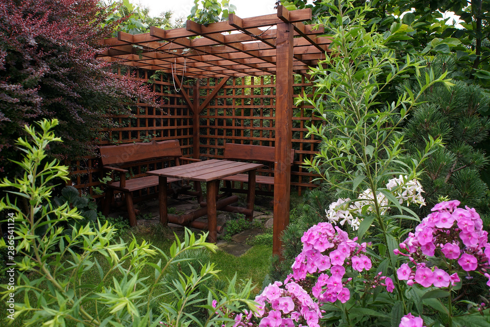 Fototapeta premium Drewniana altana ogrodowa w otoczeniu roślin i kwiatów
