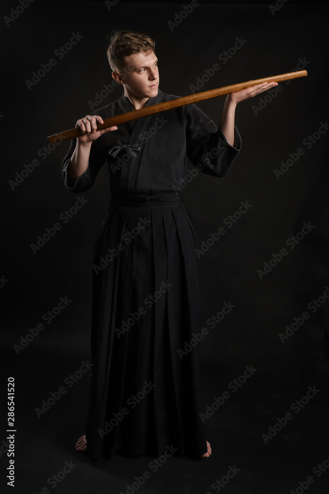 Kendo guru wearing in a traditional japanese kimono is practicing martial art with the shinai bamboo sword against a black studio background. Kendo guru wearing in a traditional japanese kimono is practicing martial art with the shinai bamboo sword against a black studio background.
