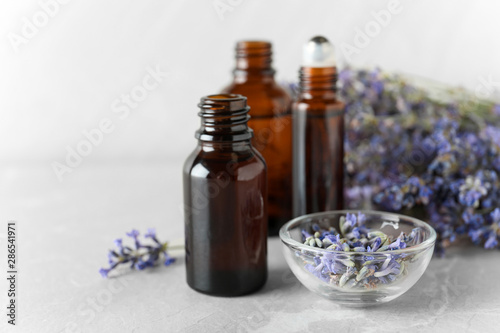 Fototapeta Naklejka Na Ścianę i Meble -  Bottles of essential oil and lavender flowers on stone table against light background. Space for text