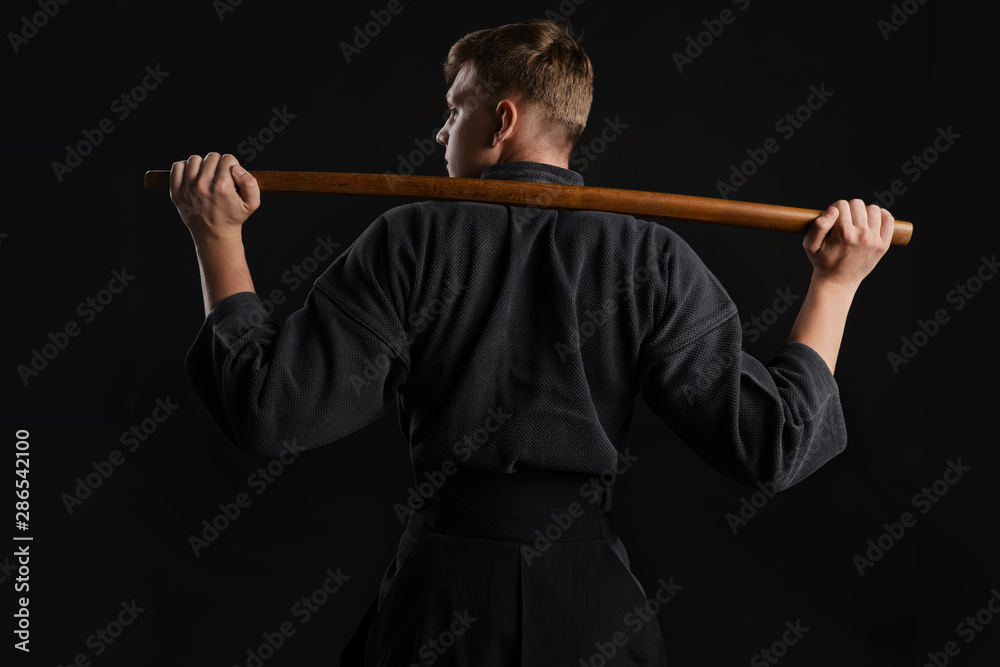 Kendo guru wearing in a traditional japanese kimono is practicing martial art with the shinai bamboo sword against a black studio background. Kendo guru wearing in a traditional japanese kimono is practicing martial art with the shinai bamboo sword against a black studio background.
