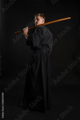 Kendo guru wearing in a traditional japanese kimono is practicing martial art with the shinai bamboo sword against a black studio background.