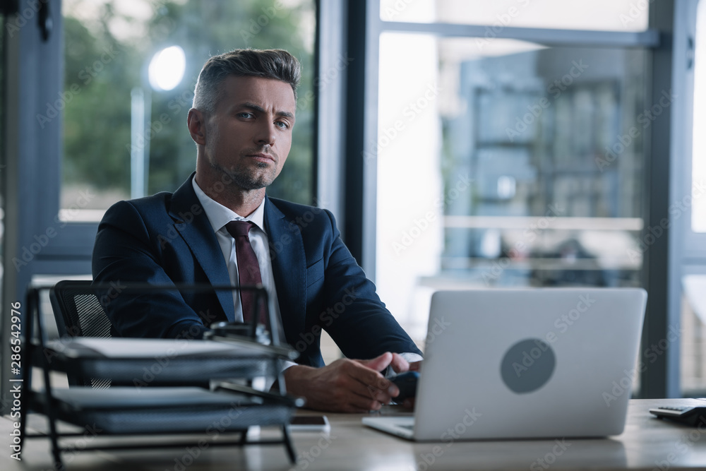 selective focus of man sitting near gadgets near document tray in office selective focus of man sitting near gadgets near document tray in office