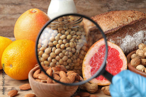 Different products with magnifier focused on jar of soy, closeup. Food allergy concept photo