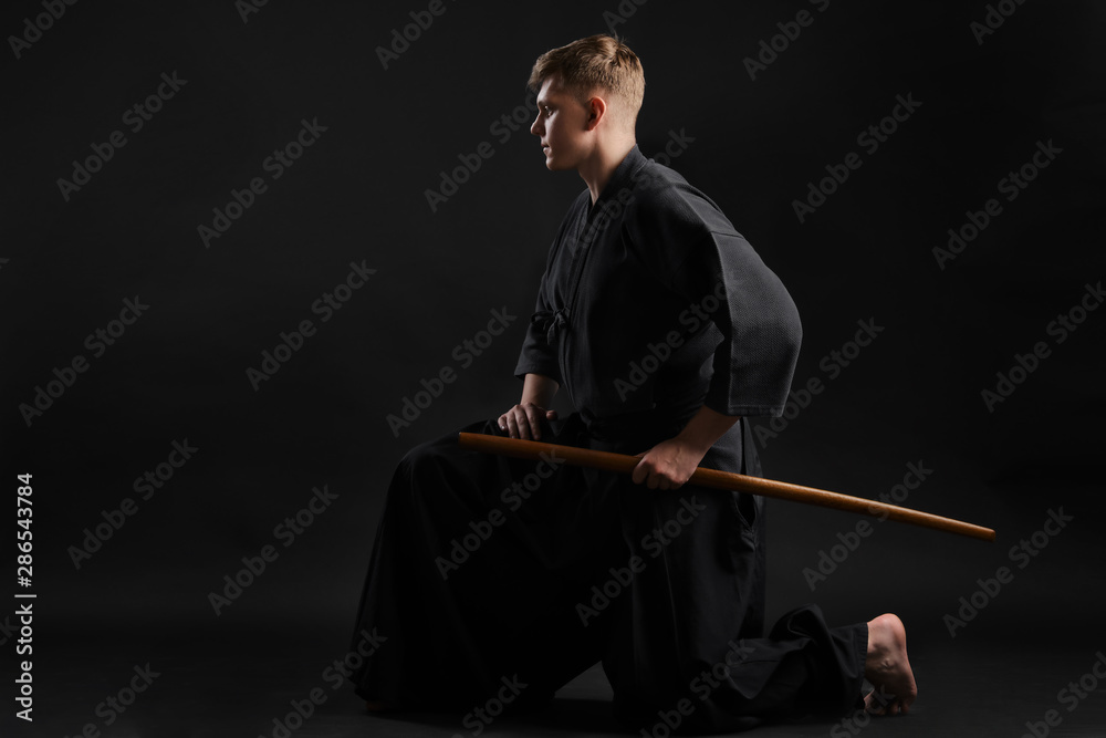 Kendo guru wearing in a traditional japanese kimono is practicing martial art with the shinai bamboo sword against a black studio background. Kendo guru wearing in a traditional japanese kimono is practicing martial art with the shinai bamboo sword against a black studio background.
