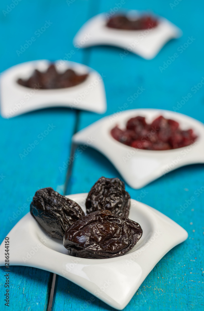 Food,taste and snack concept: dried plums in small white saucers on a wooden blue background. Food,taste and snack concept: dried plums in small white saucers on a wooden blue background.