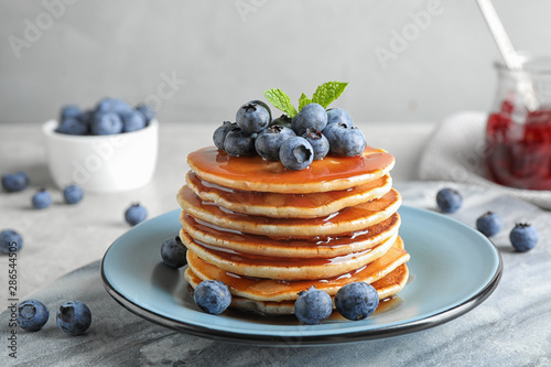 Plate of delicious pancakes with fresh blueberries and syrup on grey table against light background photo