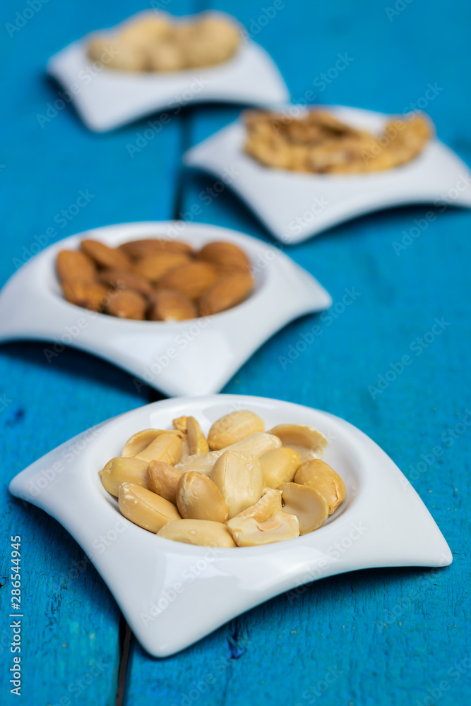 Peanuts in small white saucers on a wooden blue background. Peanuts in small white saucers on a wooden blue background.