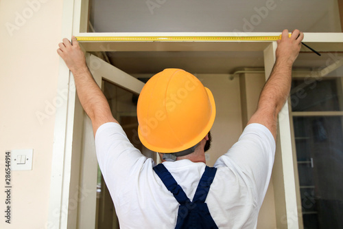 Construction worker and handyman is working on renovation of apartment. Builder is measuring of room door using measure tape at construction site. Renovation concept. Construction and service tools.