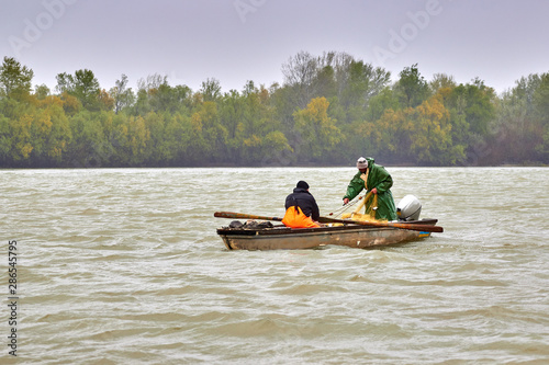 Two fisherman sort out a net full of a fish in small boat at Danube river in rainy day