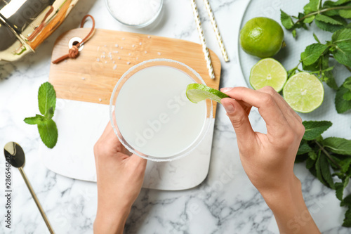 Woman decorating freshly made cocktail with lime at white marble table, top view