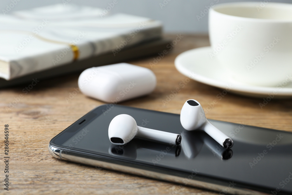 Modern wireless earphones and mobile phone on wooden table - obrazy, fototapety, plakaty 