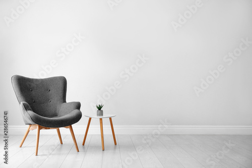 Obraz na plátně Stylish room interior with comfortable armchair near light wall, space for text