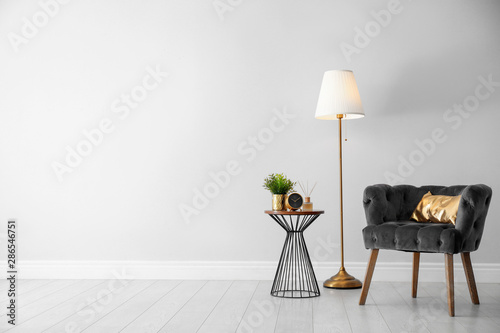 Stylish room interior with comfortable armchair, floor lamp near light wall, space for text