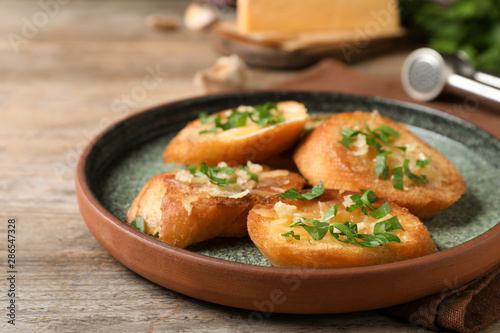Slices of toasted bread with garlic, cheese and herbs on wooden table, closeup