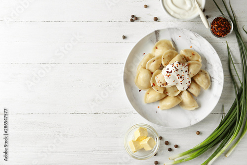 Delicious cooked dumplings with sour cream on white wooden table, flat lay. Space for text