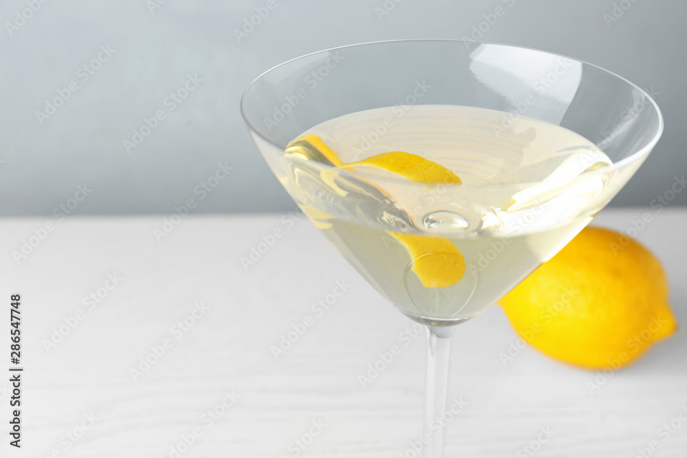 Glass of lemon drop martini cocktail with zest on white wooden table against grey background, closeup. Space for text
