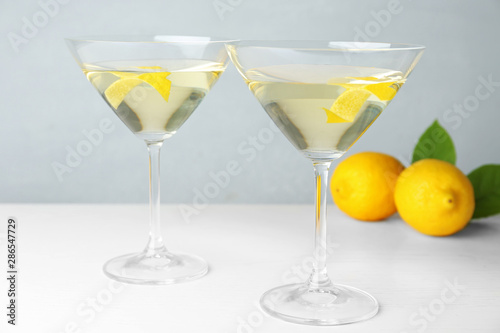 Glasses of lemon drop martini cocktail with zest on white wooden table against grey background