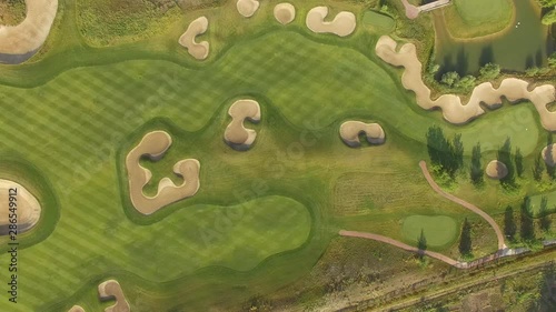 4K aerial footage of golf course. Cinematic top view shot with green grass, ponds, watercourses, palm trees, patches, holes, flags. Drone flies along the field during sunset. Vacation video concept
