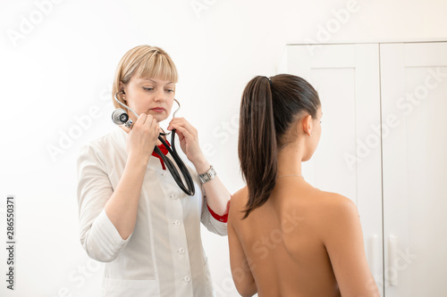 Fotografie Woman doctor therapist listening with a stethoscope to a back, young female pati