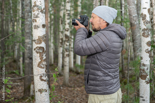 A man with a pick-up in a gray jacket, photographs nature on the banks of the river, in the forest