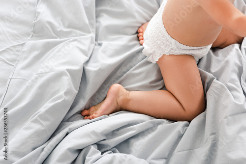 Cropped view of cute baby in diaper kneeing on white blanket