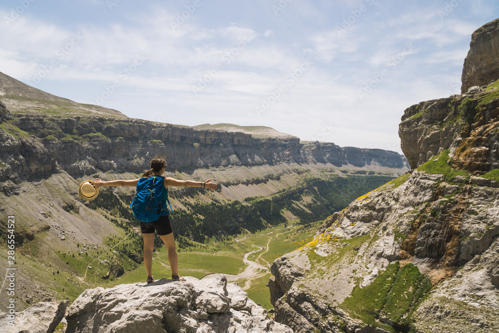 Girl backpacker hiker on the top of a cliff in the mountains watching a beautiful view of the valley, in the Pyrenees