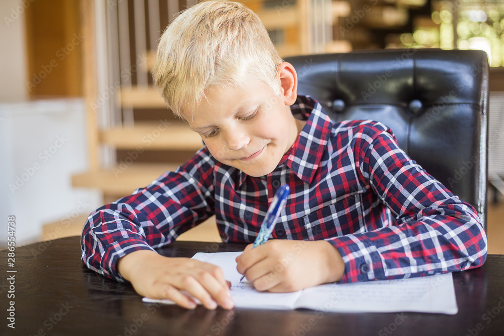 Happy schoolboy writing to notebook at home. Homework. Education, childhood and people concept Happy schoolboy writing to notebook at home. Homework. Education, childhood and people concept