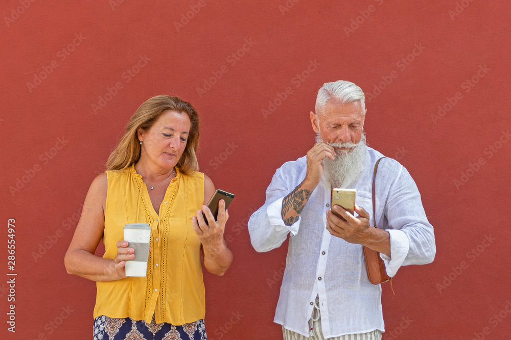 A senior couple reading their smart phones. She is holding a cardboard cup. A senior couple reading their smart phones. She is holding a cardboard cup.