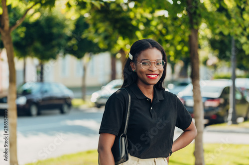 Young cool black skin girl with glasses walking in the street. © Nana_studio