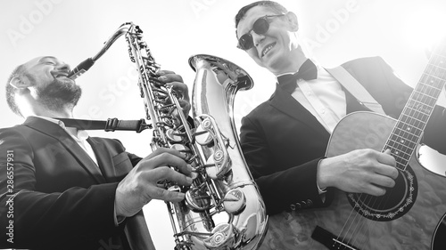 Group of two musicians  male jazz band  guitarist and saxophonist in classical costumes improvise on musical instruments in a studio black and white shot