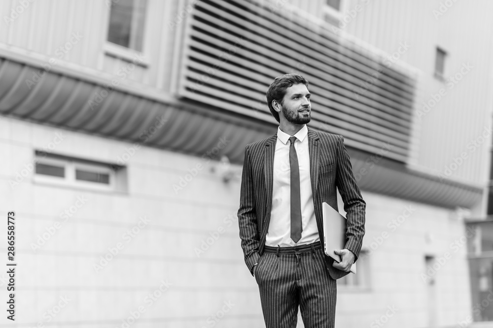Businessman with laptop walking on the city street	