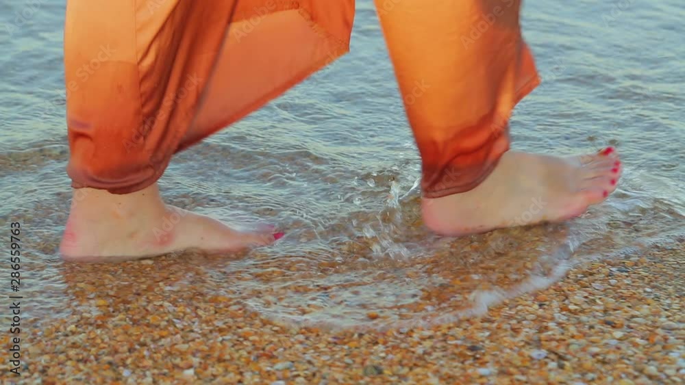 Female legs in wide trousers barefoot go along the edge of the sea water