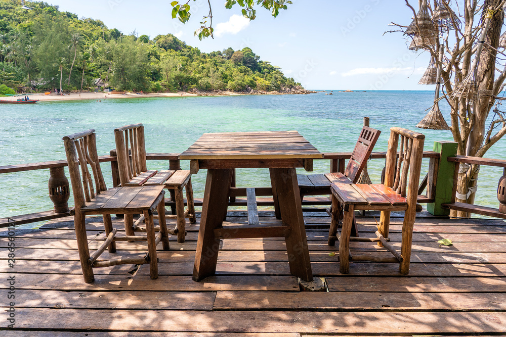 Wooden table and chairs in empty beach cafe next to sea water. Island Koh Phangan, Thailand