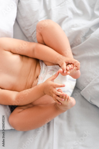 Partial view of little baby in diaper laying on back and touching feet with hands