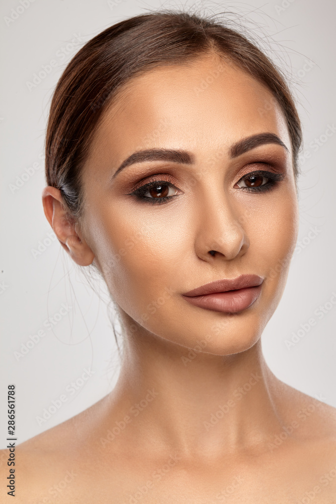 Close up portrait of a brunette nude model girl with professional evening make-up and plump lips, posing on gray background. Close up portrait of a brunette nude model girl with professional evening make-up and plump lips, posing on gray background.