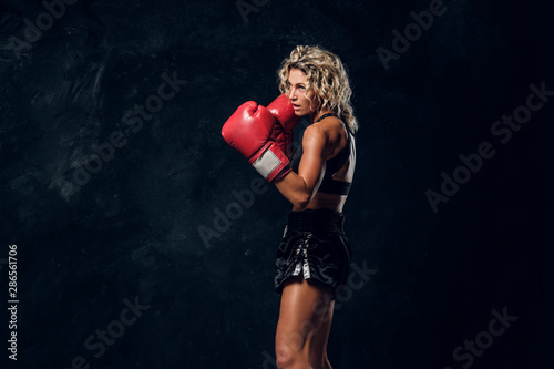 Sportive muscular woman is demonstrating her boxing exercises, wearing gloves.