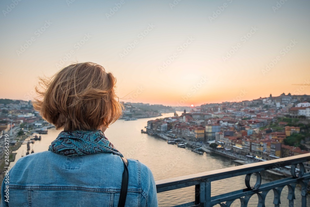 redhead woman observing the sunset in porto, portugal on the bridge over the river