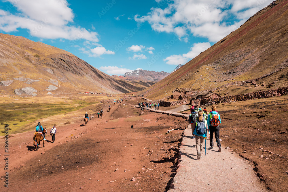 Tourists walking to Vinicunca Rainbow Mountain through stunning barren mountain landscape, Peru