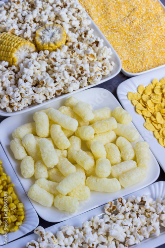 A set of products made from corn: popcorn, sticks, cereal, and corn grits. White plates
