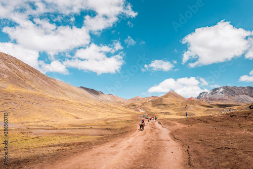 Tourists walking to Vinicunca Rainbow Mountain through stunning barren mountain landscape  Peru
