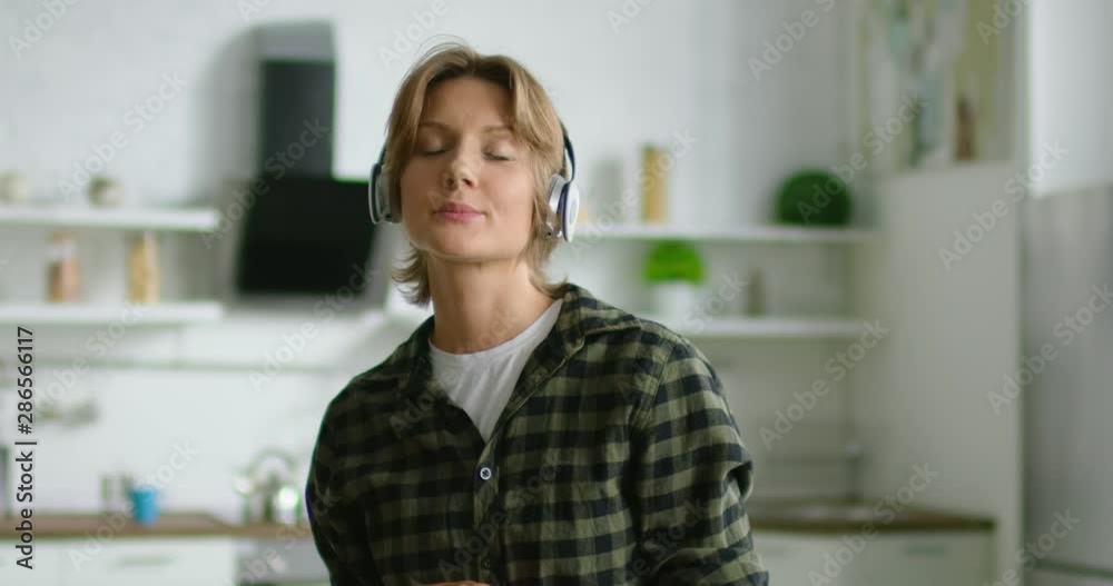 Young woman, student, girlfriend, in positive mood is listening music in wireless headset, relaxing, closed eyes, enjoying free time at home. Caucasian, brunette, grey eyes, indoor. 4K, RED camera. Young woman, student, girlfriend, in positive mood is listening music in wireless headset, relaxing, closed eyes, enjoying free time at home. Caucasian, brunette, grey eyes, indoor. 4K, RED camera.