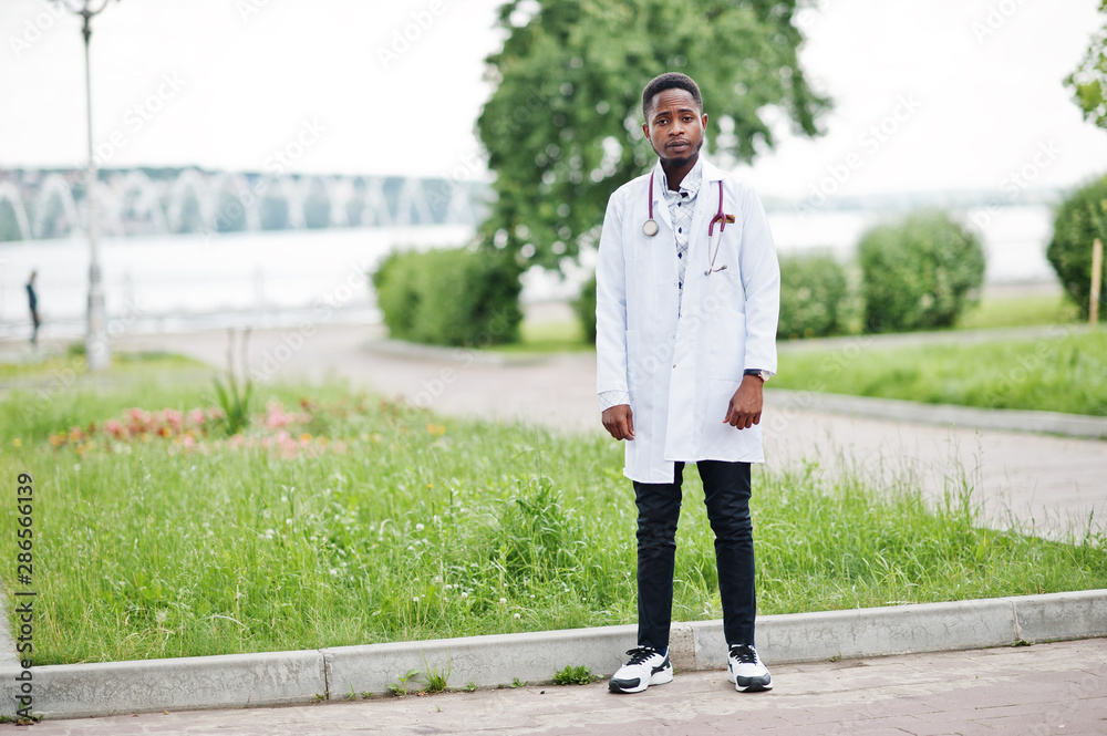 Young african american male doctor in white coat with a stethoscope posed outdoor.