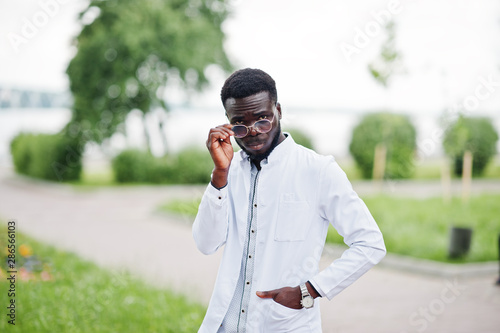 Young african american male doctor in white coat with a stethoscope posed outdoor.