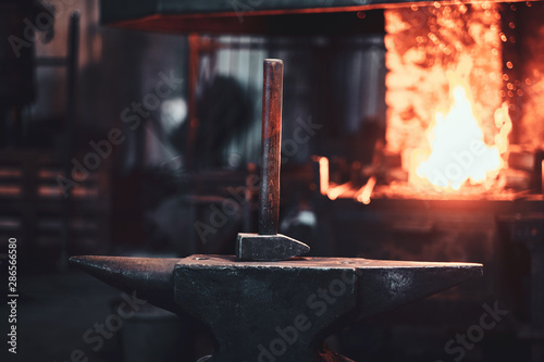 Fotografia Hammer on anvil at dark blacksmith workshop with fire in stove at background
