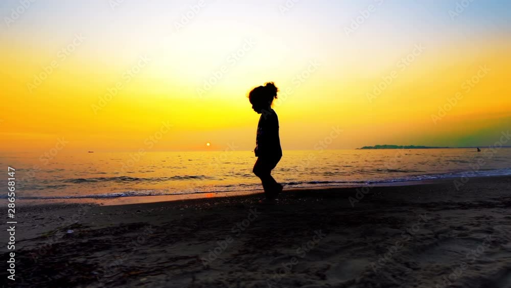 Silhouette of young boy walking on an empty beach with summer sunset at background, cinematic steadicam shot Silhouette of young boy walking on an empty beach with summer sunset at background, cinematic steadicam shot