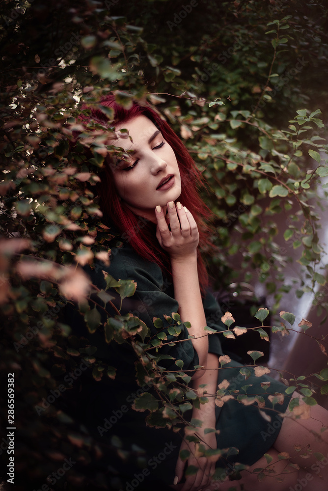 Young fashionable woman in romantic green dress and red hair, posing near houses in park. Young fashionable woman in romantic green dress and red hair, posing near houses in park.